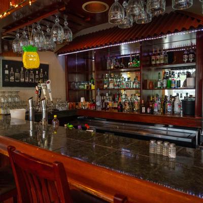 A dimly lit bar featuring wooden stools, liquor bottles, and hanging glassware.
