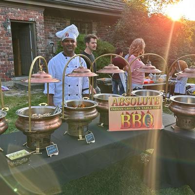 Chef standing by an outdoor Indian grill buffet table with chafing dishes.