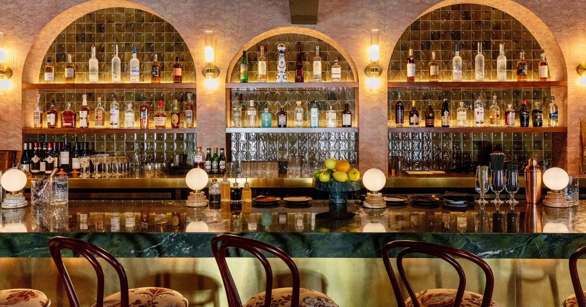 Modern bar with seating, marble counter, and warmly lit arched liquor shelves