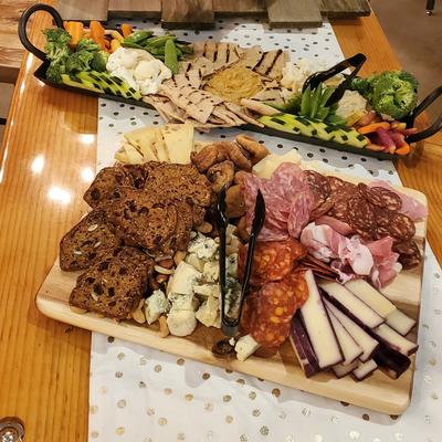 A wooden table holds a colorful charcuterie board and a hummus plater.