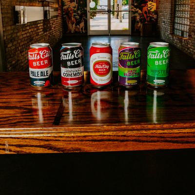 Five cans of Falls City Beer on a wooden table in an indoor setting..