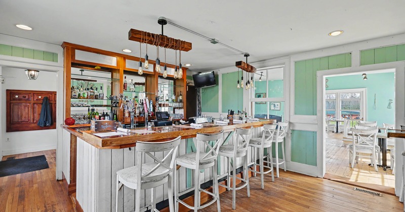 Bright, rustic bar area with wooden floors, white bar stools, and mint green walls