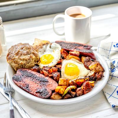 A breakfast plate with eggs, sausages, potatoes, and a biscuit, beside a mug of coffee.