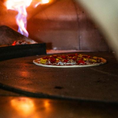 Pizza baking in a wood-fired oven with visible flames in the background.