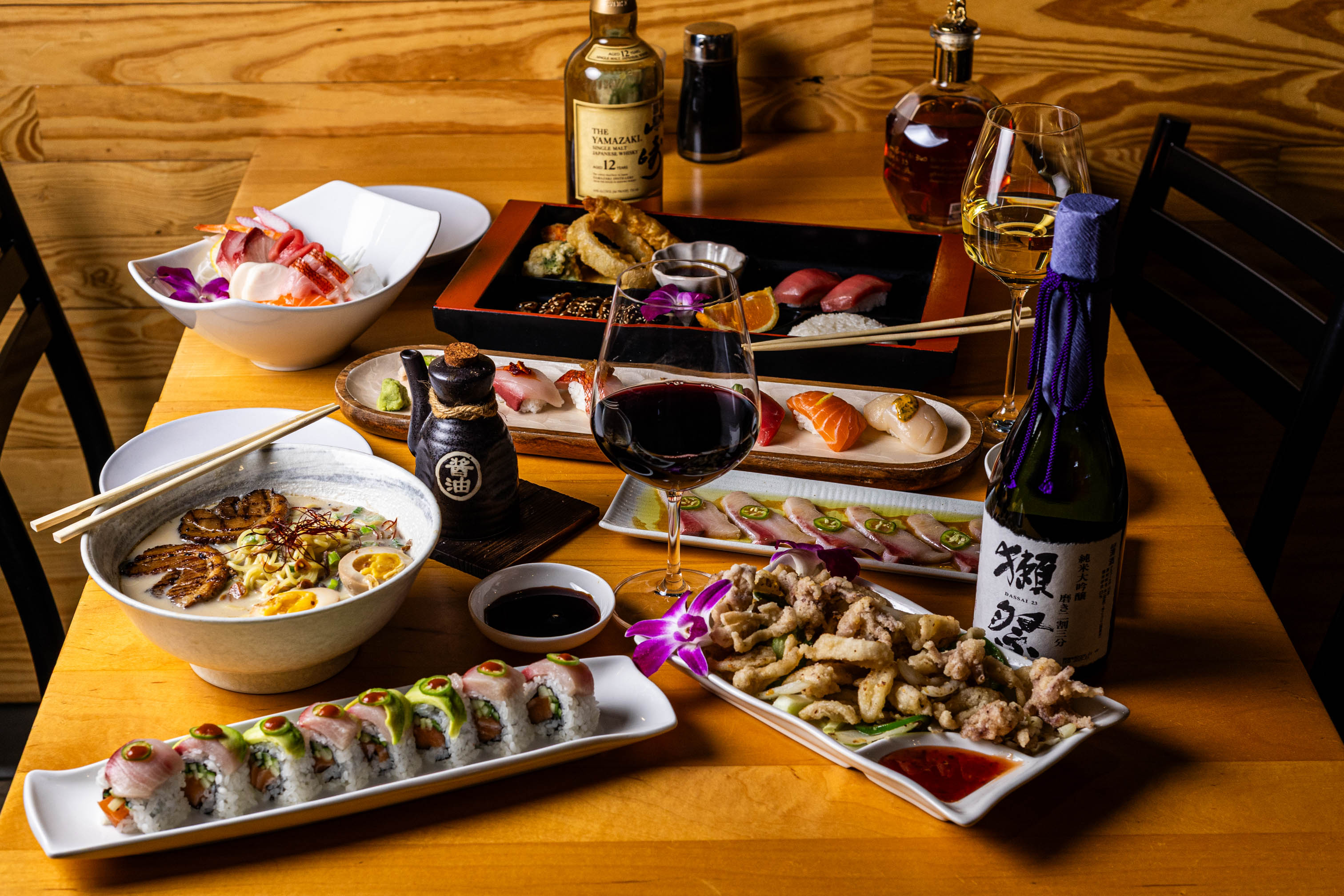 Table filled with sushi, sashimi, ramen, and wine