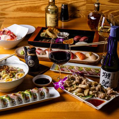 Table filled with sushi, sashimi, ramen, and wine.