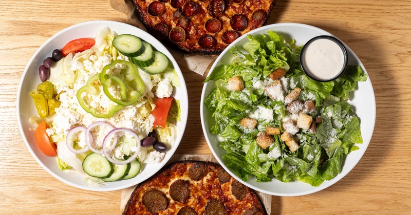 Top view, clockwise motion - pepperoni pizza, Caesar salad, meatball pizza, and Greek salad