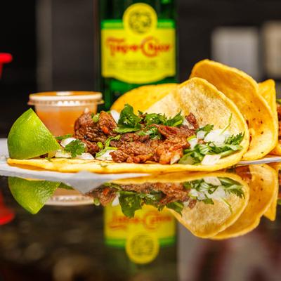 Mixed Taco Plate with a lime wedge and a diping sauce, alongside a bottle of soda.
