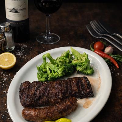 Grilled steak served with a grilled sausage, salted broccoli florets, and red wine..