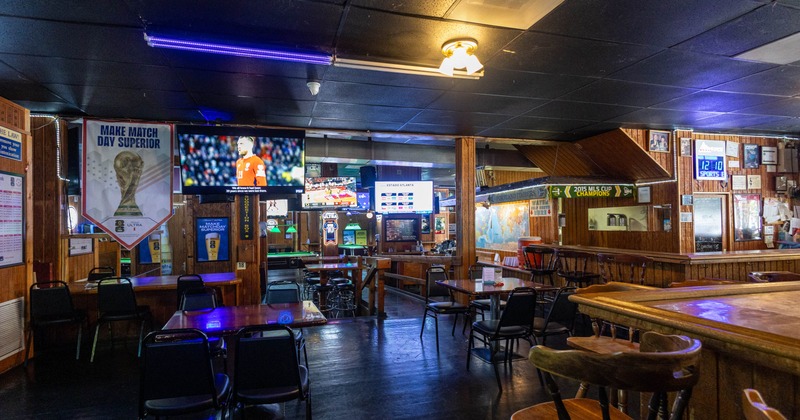 Interior of a sports bar with tables, chairs, and multiple screens showing sports broadcasts