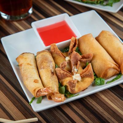 Assorted Asian appetizers with crispy spring rolls, fried wontons, and red dipping sauce.