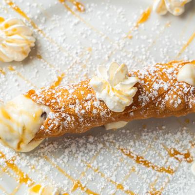 Cannoli with whipped cream, caramel sauce drizzle, and powdered sugar.