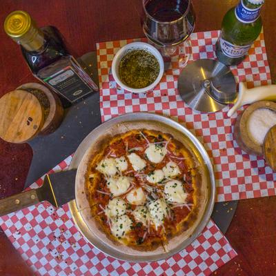 Margherita pizza surrounded by drinks, condiments, and a pizza cutter.