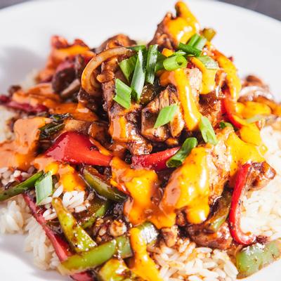 Jerk chicken, onions, and peppers over white rice, topped with chipotle aioli sauce