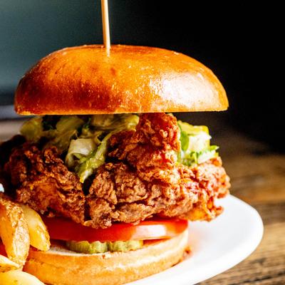 Buffalo fried chicken sandwich with lettuce, pickles, and tomatoes, served with fries.