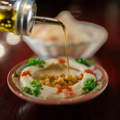 Olive oil being drizzled over hummus topped with chickpeas and paprika.