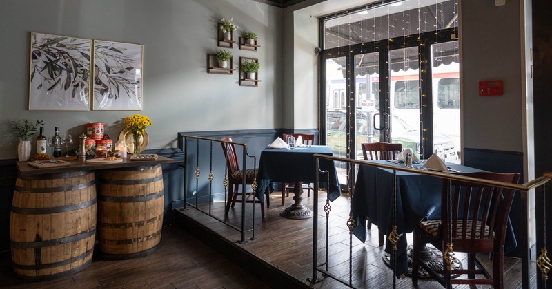 A restaurant interior with barrel-supported table, dining tables with dark tablecloths, artwork