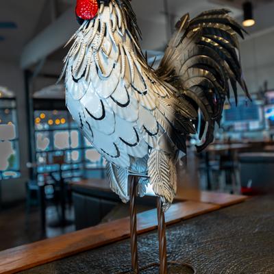 A metallic rooster sculpture with shiny feathers, standing on a wooden counter.