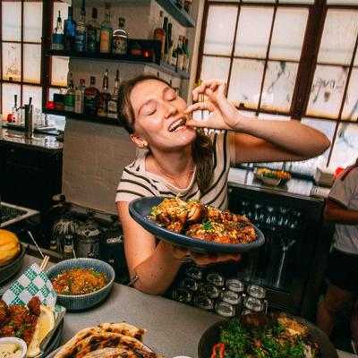 A smiling person eats food from a plate in a restaurant setting.