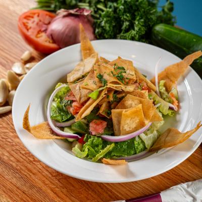 Fattoush salad topped with crispy pita chips served on a table with fresh veggies nearby.