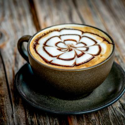 Cappuccino, with coffee art, served in a ceramic cup on a rustic wooden table.