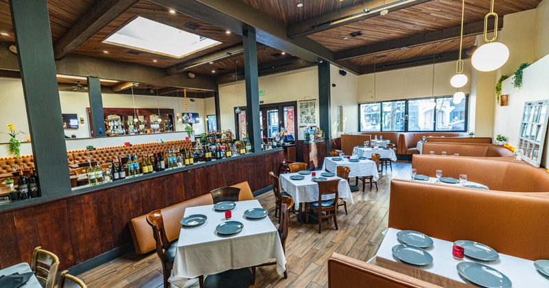 Interior of a modern restaurant with white tablecloths, booth seating, a long bar