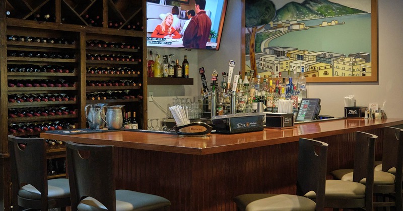 A wooden bar with stools in front, wine rack and a large framed painting of Naples