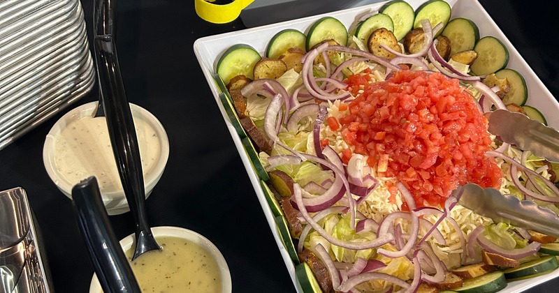 A large salad in a white serving dish, accompanied by separate bowls of dressing
