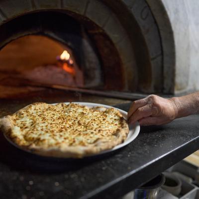 A freshly baked pizza being removed from a traditional wood-fired brick oven.