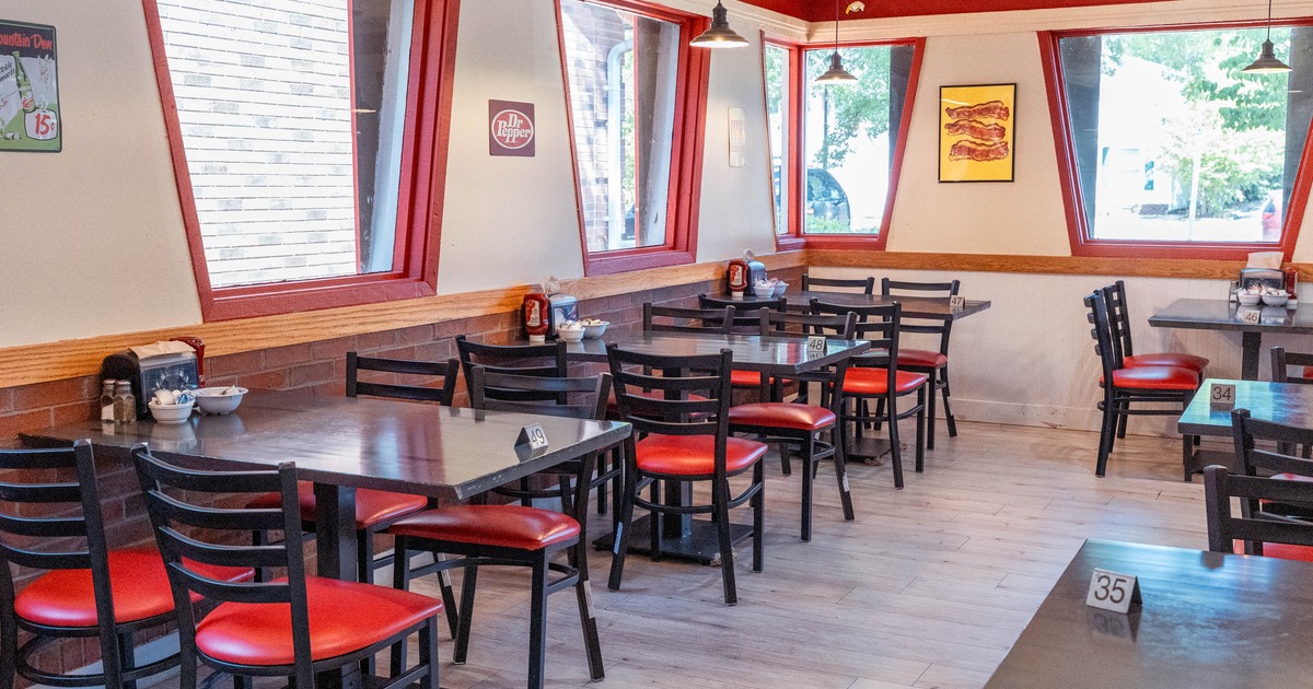 A casual restaurant with tables, red-cushioned chairs, large windows and vintage decor.