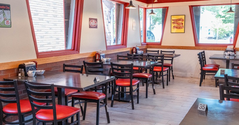 A casual restaurant with tables, red-cushioned chairs, large windows and vintage decor.