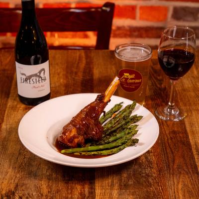 Lamb Shank with asparagus on a white plate, accompanied with red wine and beer.