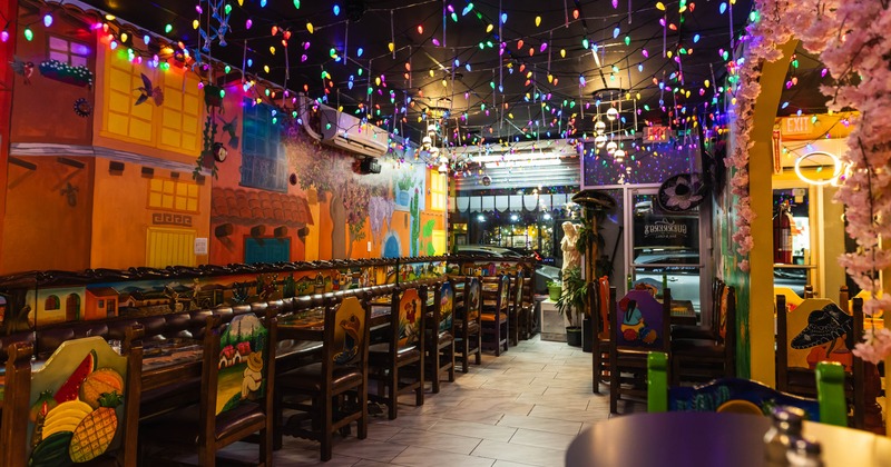Festive restaurant interior with colorful string lights, murals, decorated chairs, and cherry blossom accents