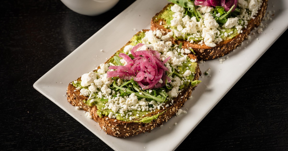 Avocado toast topped with crumbled cheese and pickled red onions