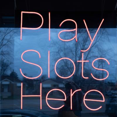 Neon window sign reading Play Slots Here.