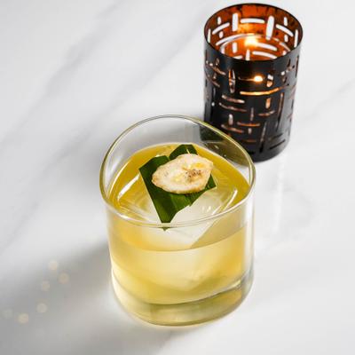Clear cocktail garnished with banana leaf and dried banana slice.