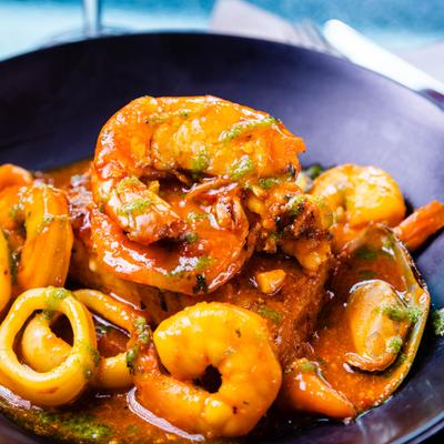 Spanish seafood stew featuring fried fish, shrimp, calamari, and mussels in tomato-based sauce.