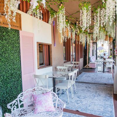 Outdoor cafe patio with hanging white flowers, green walls, and furniture.
