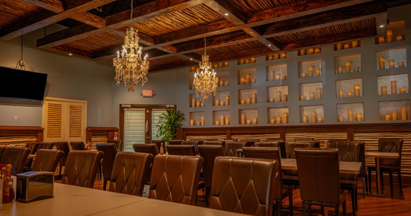 A restaurant dining area with chandeliers, candle-lit shelves, and dark brown chairs and tables