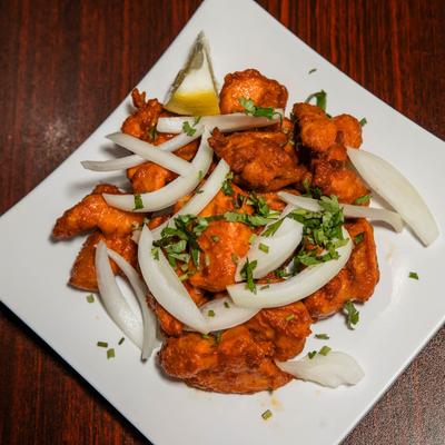 Spicy fried chicken pieces garnished with sliced onions, chopped cilantro, and a lemon wedge.