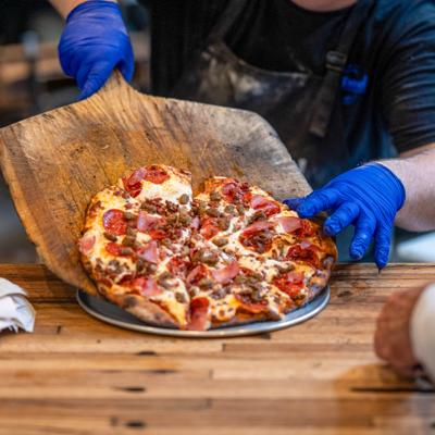 Pizza chef sliding a meat lovers pizza from a wooden peel onto a metal tray.
