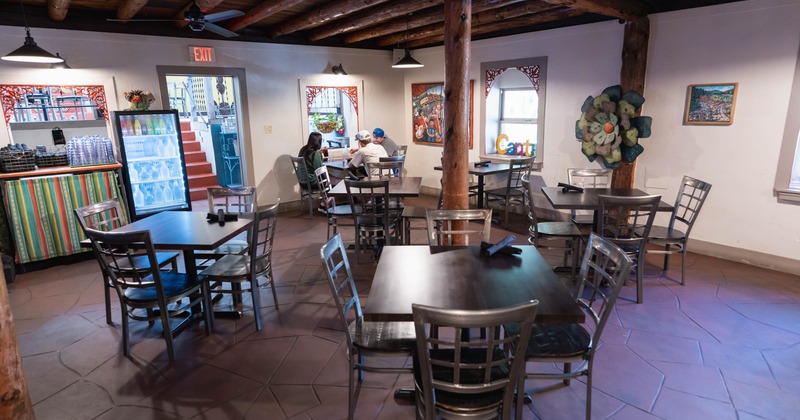 Interior of a rustic restaurant with tables, chairs, artwork, and a drink refrigerator