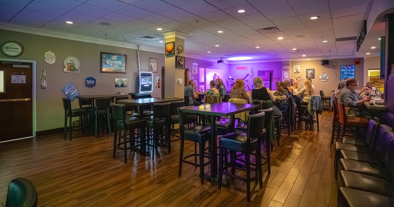 Interior seating area with high tables and stools, and a bar with guests sitting at the bar counter