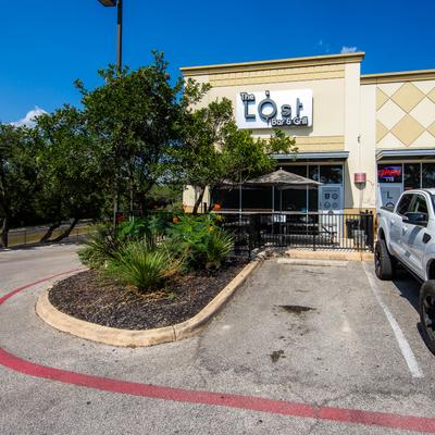Restaurant's exterior with signage, trees and plants in front of it.