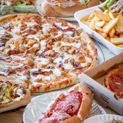 Large chicken bacon ranch pizza surrounded by various sandwiches and fries.