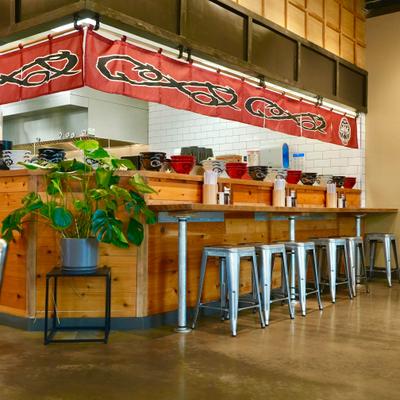 Bar area with wooden counter, metal stools and a red curtain with a sign.