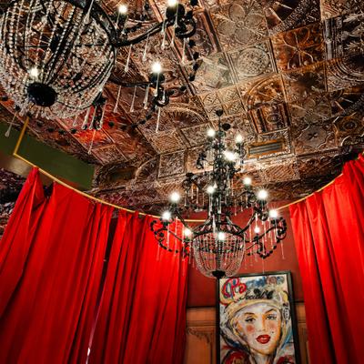 Chandeliers hanging of ceiling above red curtains and wall art.