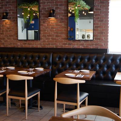 A brick wall with mirrors, black tufted banquette, chairs, and tables set for meal.