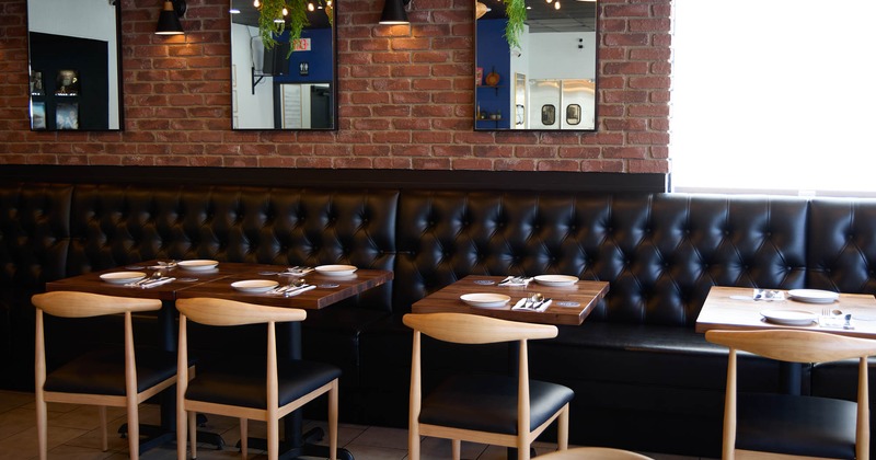 A brick wall with mirrors, black tufted banquette, chairs, and tables set for meal