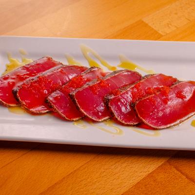 Pepper crusted seared tuna arranged on a white plate with drizzle of sauce.
